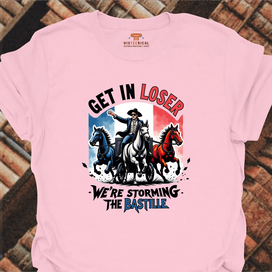 Pink t-shirt with graphic design of a man on horseback and text 'Get in Loser, We're Storming the Bastille' on a brick background.