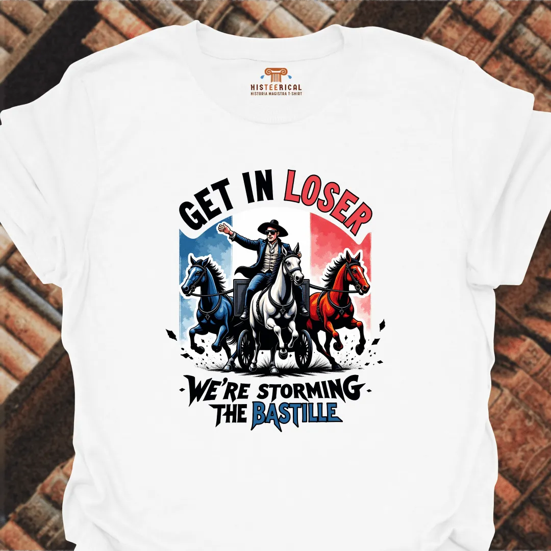 White t-shirt with graphic design of a man on horseback and text 'Get in Loser, We're Storming the Bastille' on a brick background.