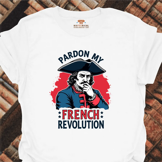 White t-shirt with a graphic of a historical figure and text 'Pardon My French Revolution' on a brick background.